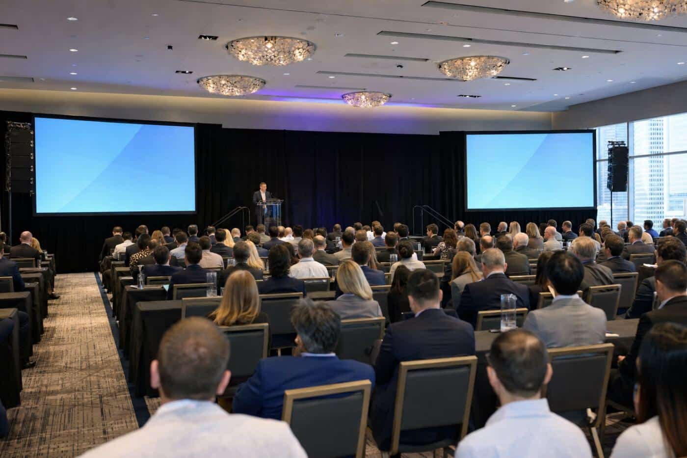Hotel ballroom set up for a corporate conference with a podium, two projection screens and line array speakers